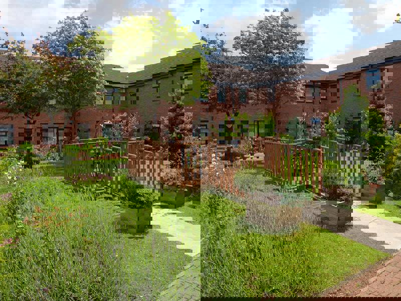 A view of a wooden deck in a garden with a red brick home in the background