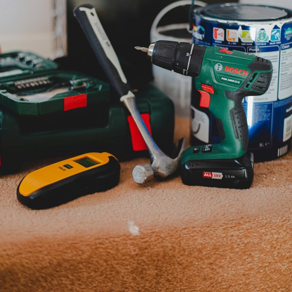 A hammer, drill, paint can and other tools on a carpeted stair