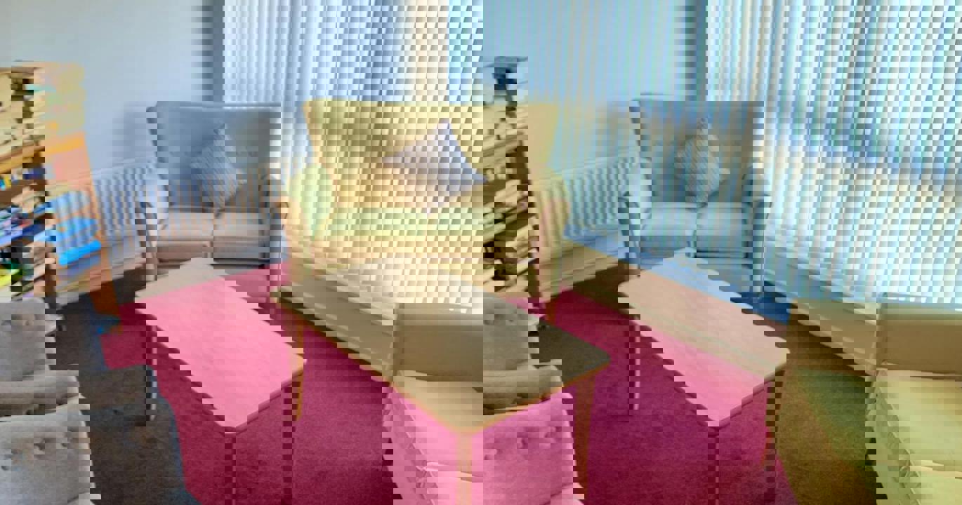 A cosy reading room with two small yellow sofas, a coffee table and a bookshelf filled with books