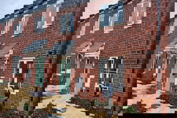 A two-storey red brick housing development with a sage-coloured front door and newly planted flower beds