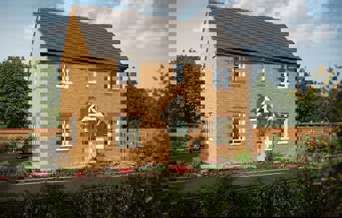 A large, two-storey home with lots of windows and a light green door way surrounded by blooming flower-beds